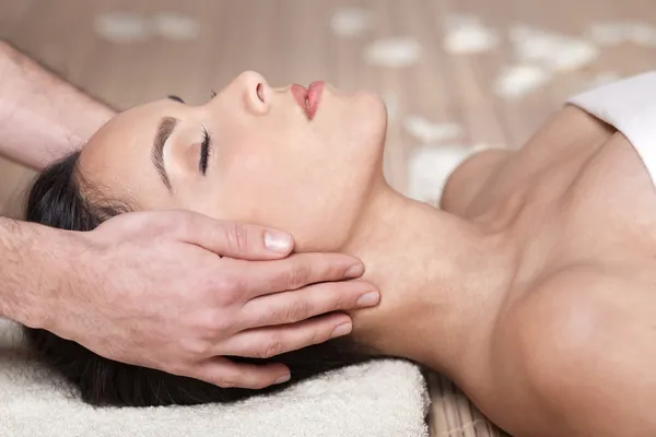 Un masseur masse le visage d'une jeune femme à l'occasion d'un massage relaxant de l'ensemble du corps.